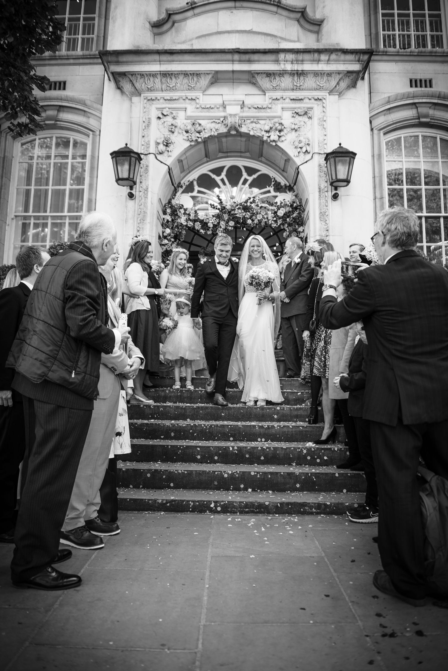 Black and white photo of bride and groom descending steps through confetti shower at wedding.  London Wedding at Chelsea Town Hall.