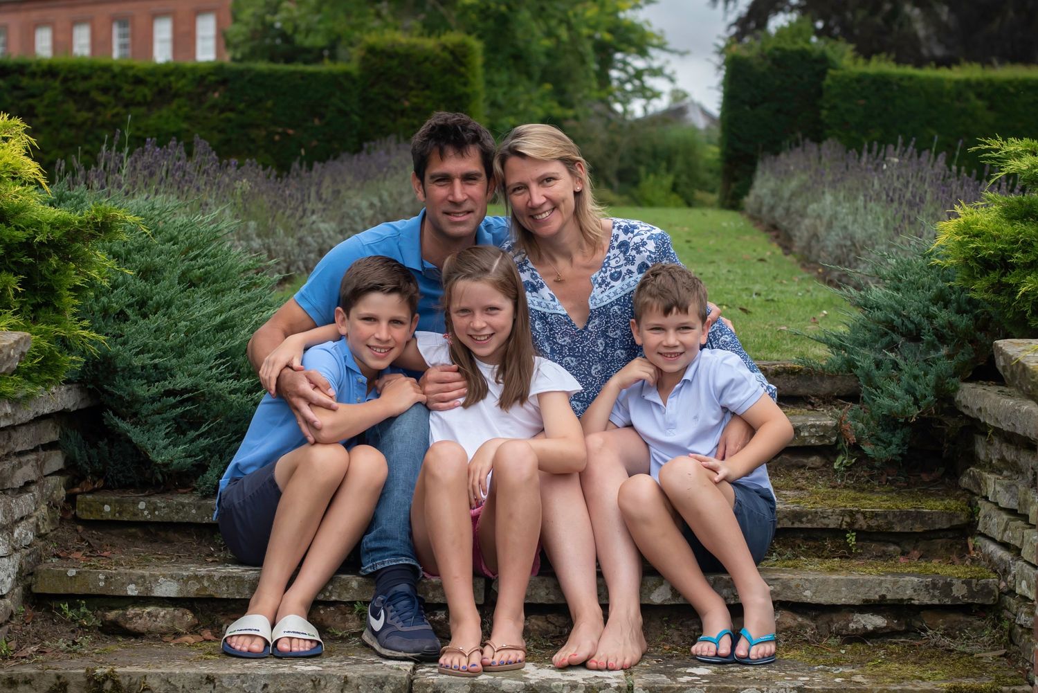 Family of five sitting on stone steps in garden, parents with three children smiling at camera.