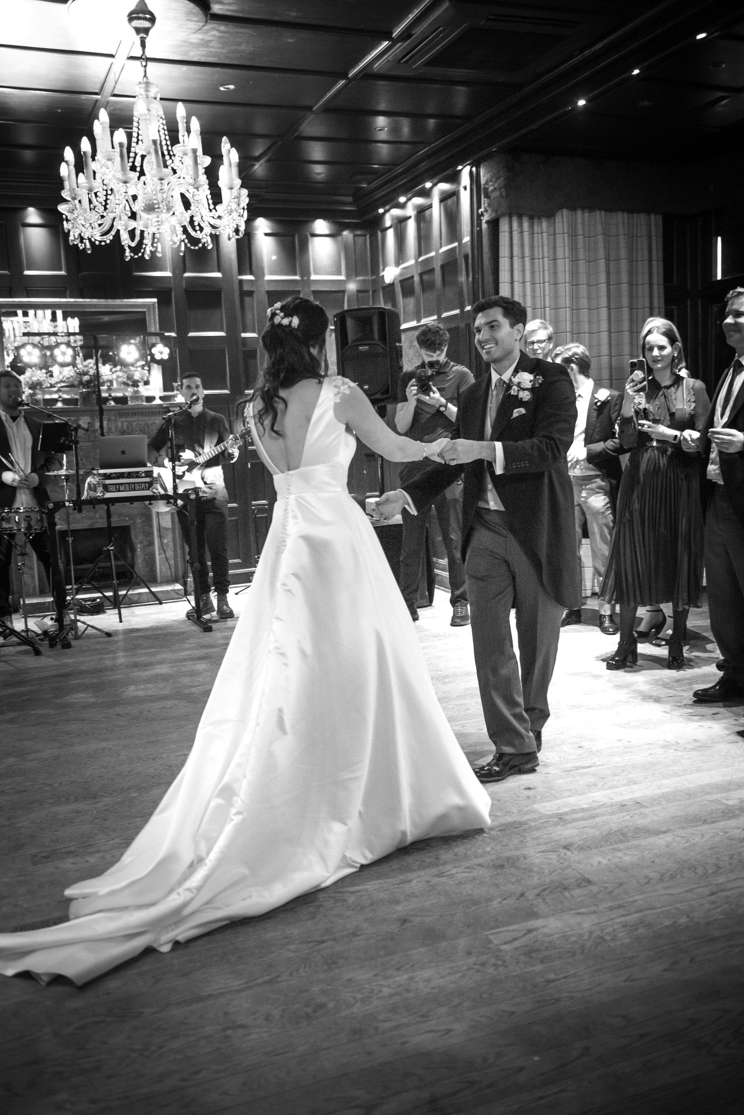 Bride in a flowing white gown and groom share a romantic first dance under a crystal chandelier.