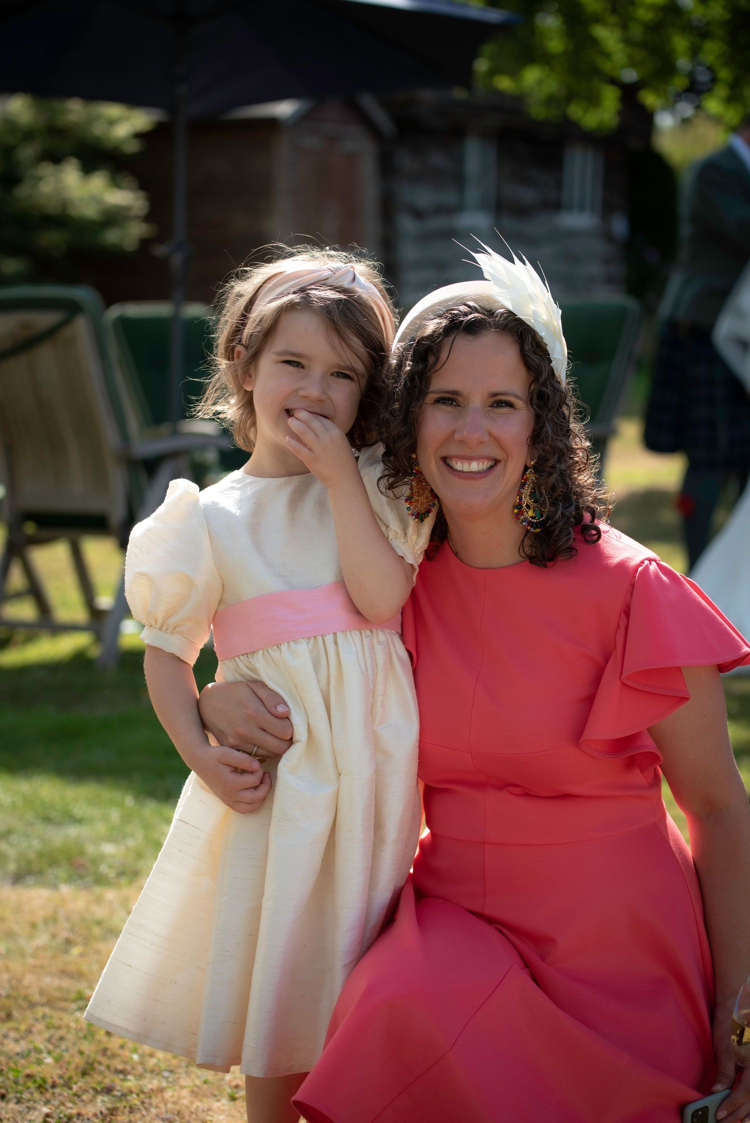 Smiling woman in pink dress posing with young flower girl in cream dress at wedding.