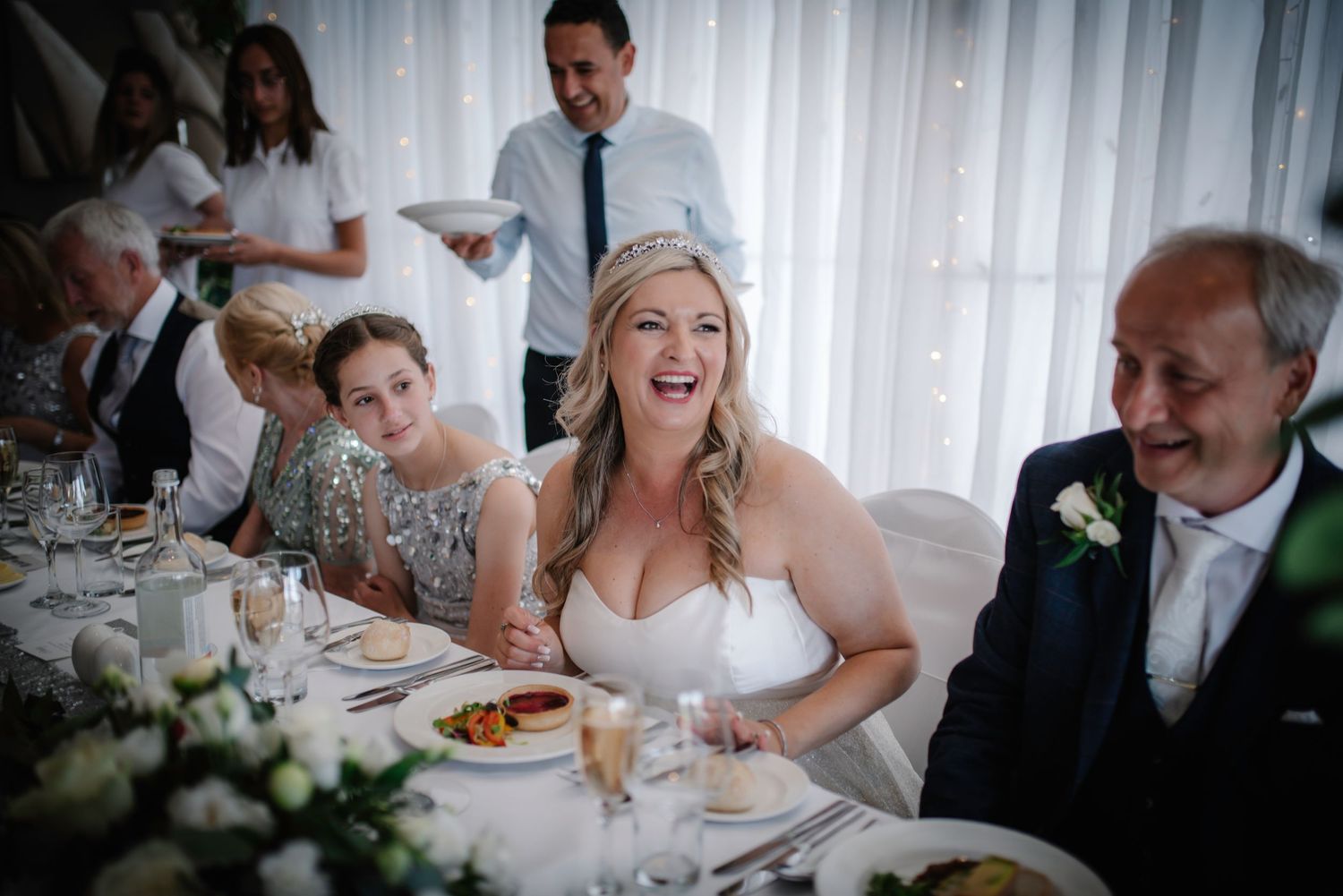 Bride laughing joyfully with guests at the wedding reception dinner table.