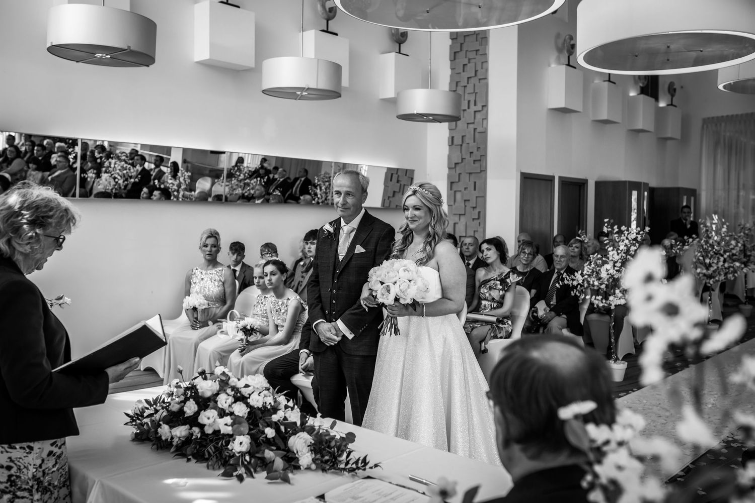 Bride and groom standing at altar during wedding ceremony with floral arrangements in bright venue.