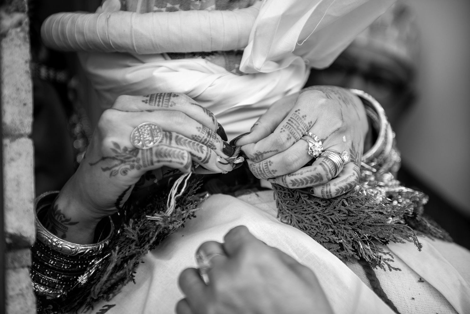 Close-up of hands adorned with henna, rings, and bangles during a traditional wedding ritual.