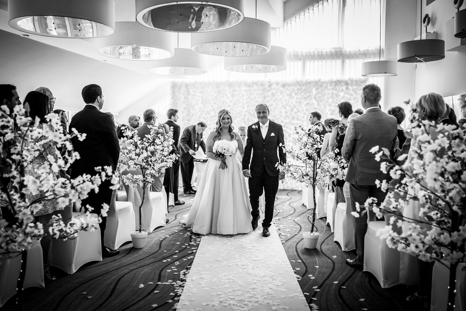 Newlyweds joyfully walking down decorated aisle lined with cherry blossom arrangements after ceremony.