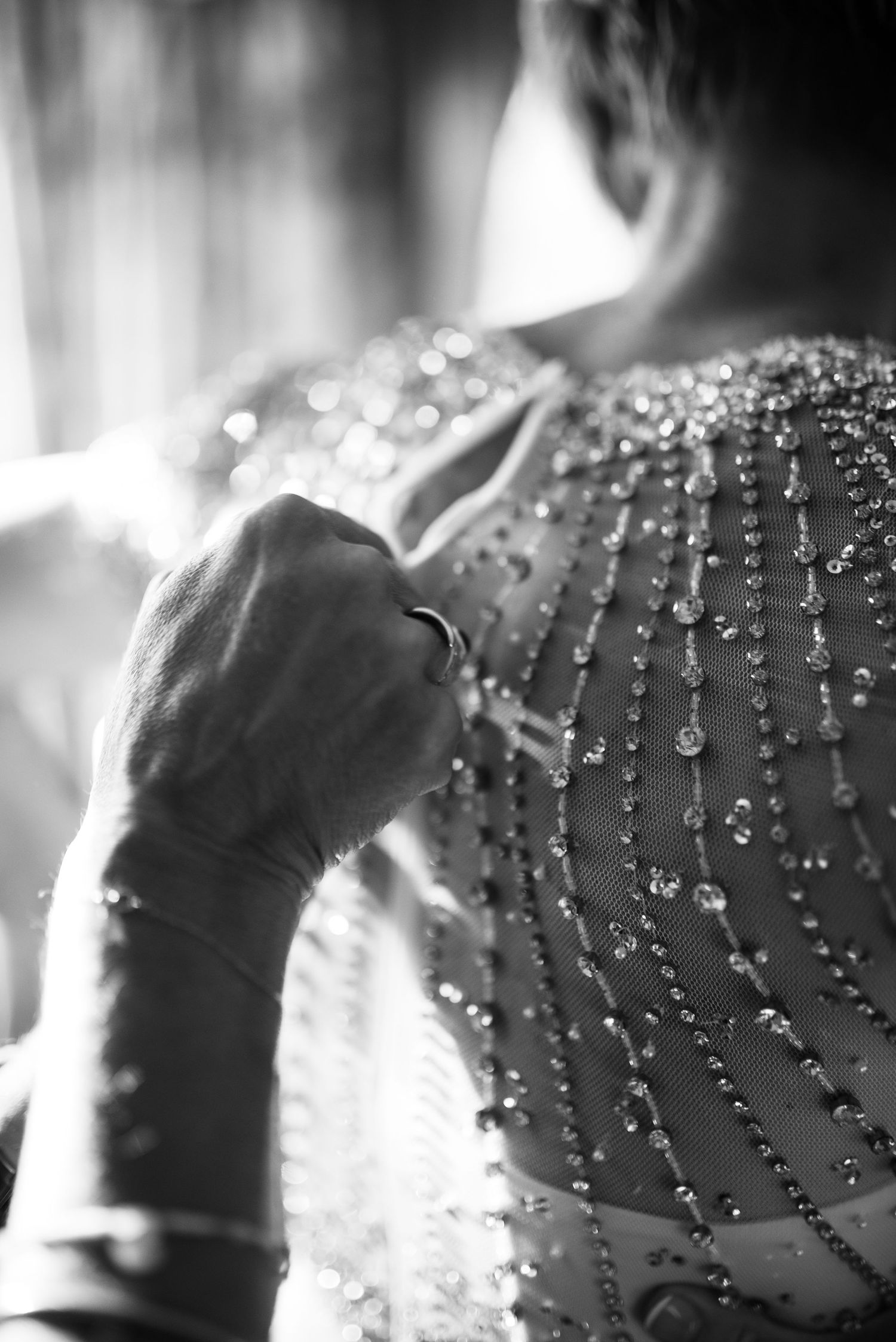 Close-up black and white photo of beaded wedding dress back with intricate crystal embellishments and ring detail.