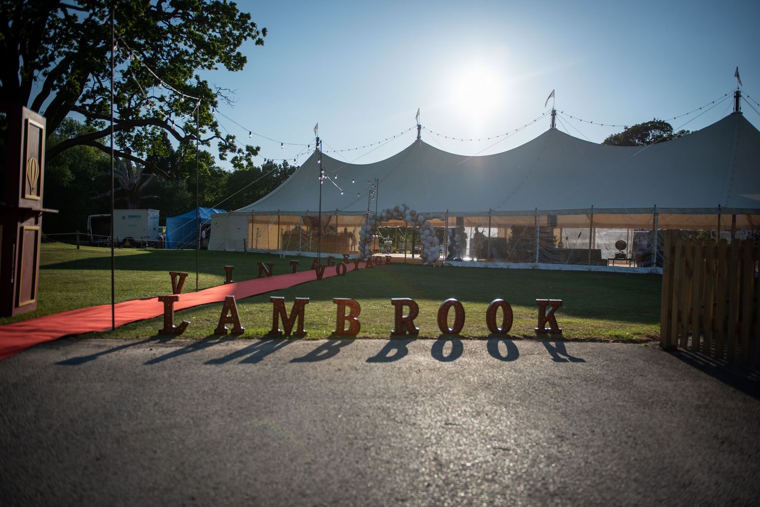 Illuminated Lambrook sign at entrance of white marquee tent venue at dusk.