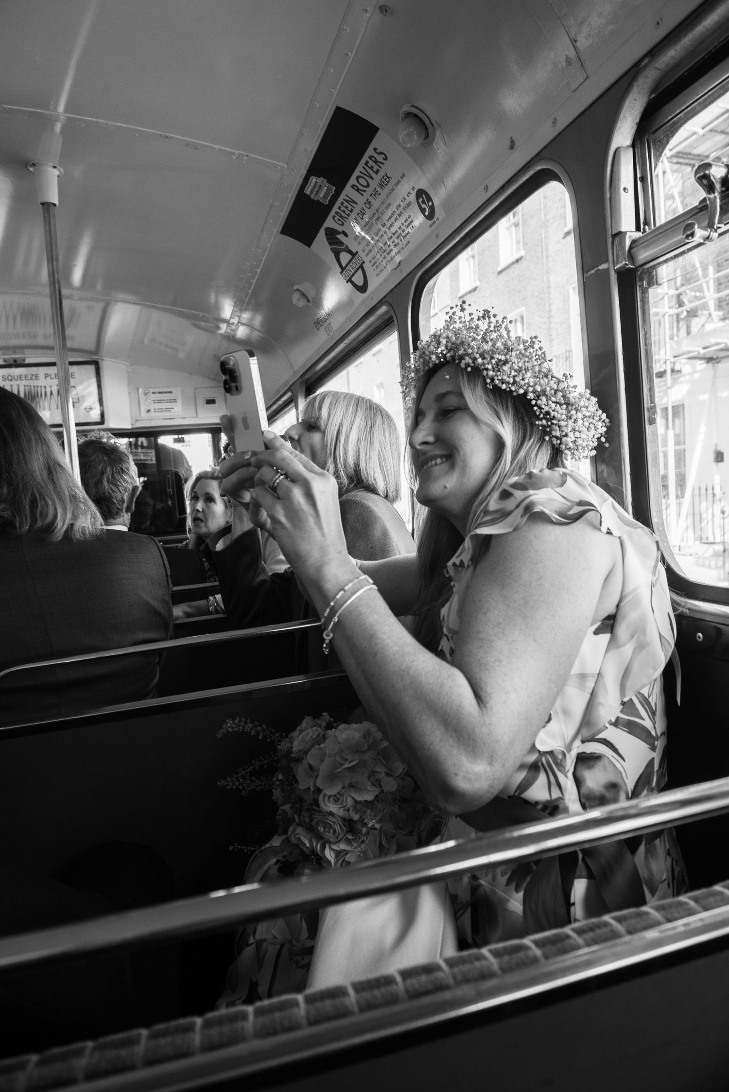 Wedding guest wearing floral crown smiling and taking photo inside vintage double-decker bus. London wedding.