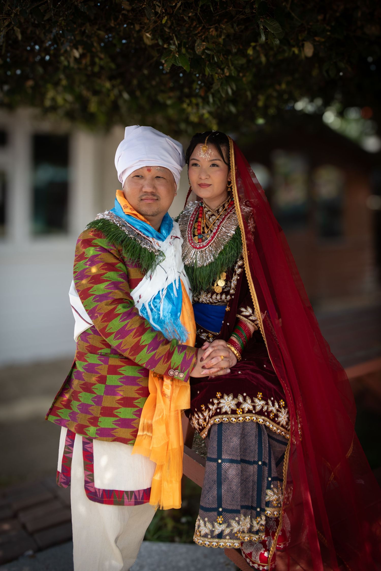 Couple in colorful traditional Nepali wedding attire posing together outdoors.