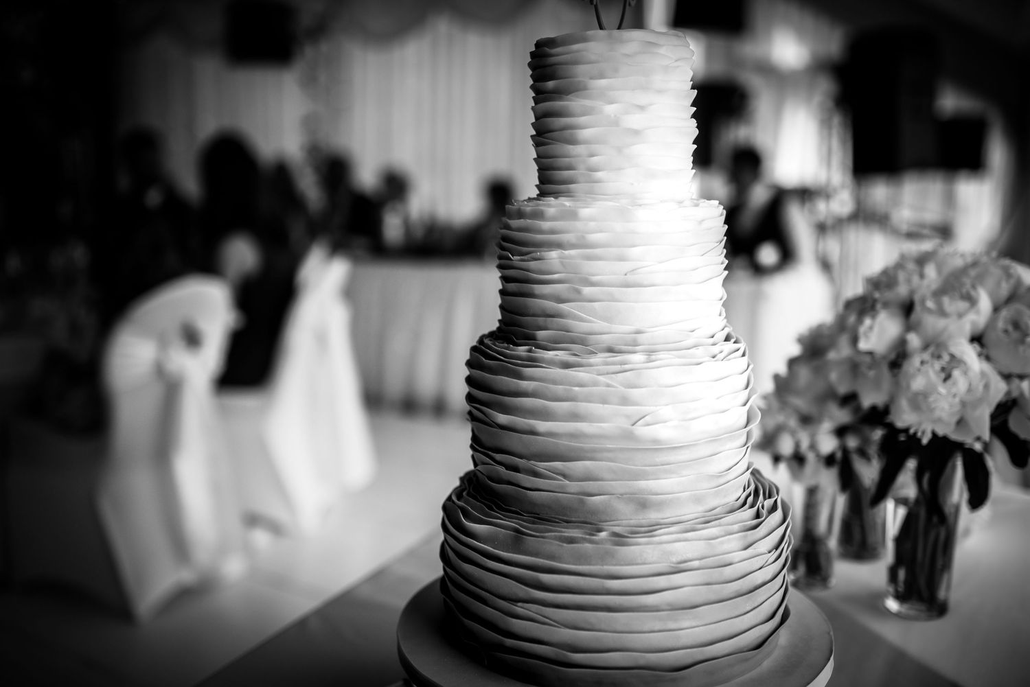 Stunning four-tier ruffled wedding cake in black and white with floral arrangements.