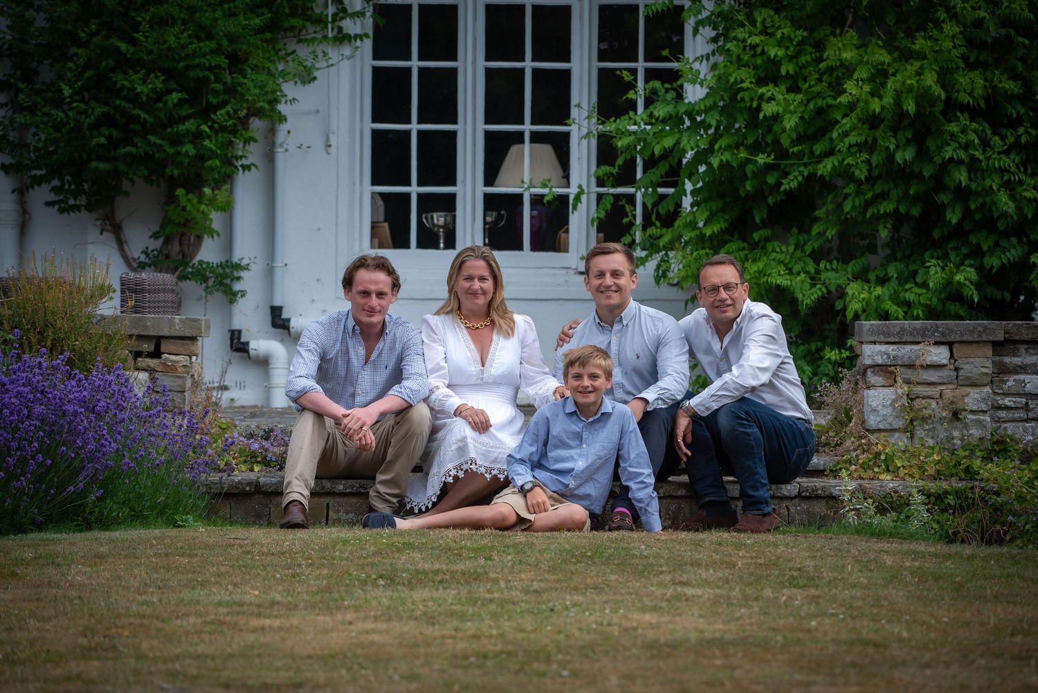 Family of five posing together outside elegant white house with garden. family portrait