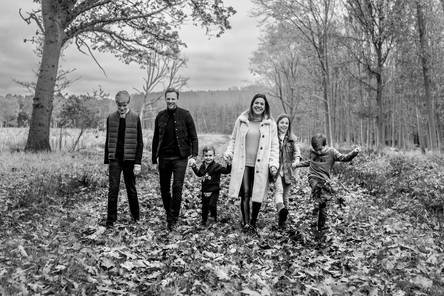 Black and white family portrait with parents and four children standing in autumn woodland.