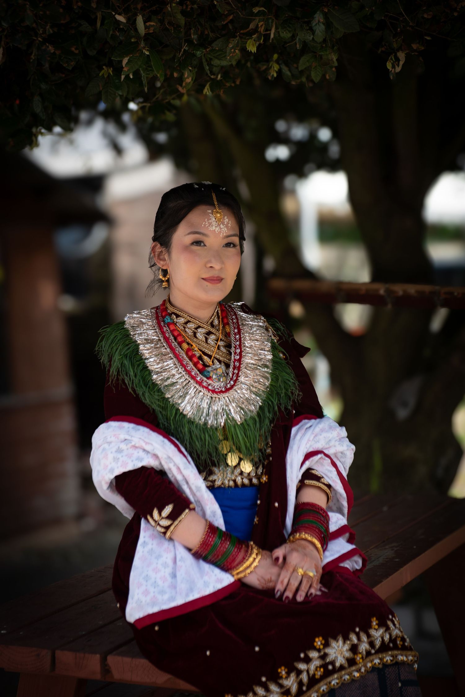 Young woman wearing traditional cultural attire with ornate jewelry and headdress seated outdoors.