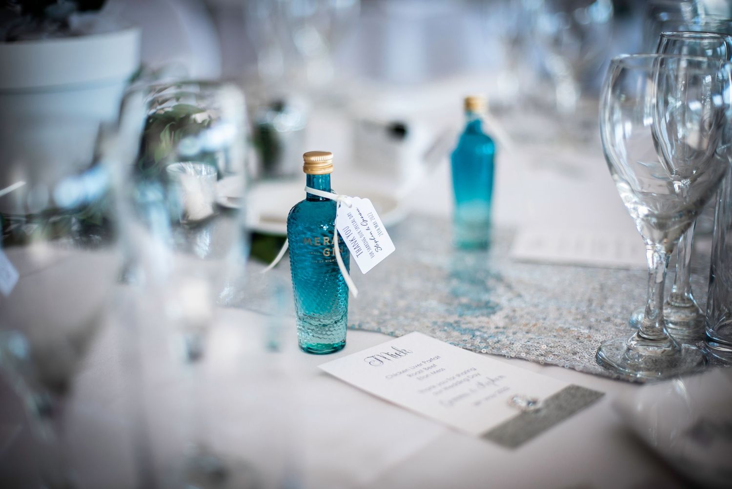 Small blue decorative gin bottle with tag sits on elegant wedding reception table setting.