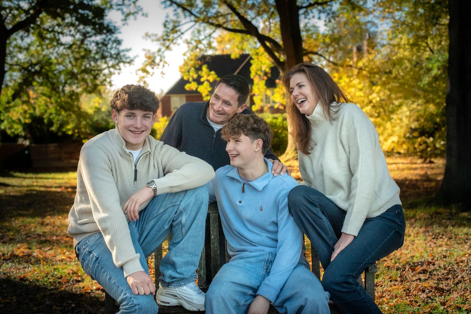 A happy family of four laughs together outdoors surrounded by golden autumn foliage.