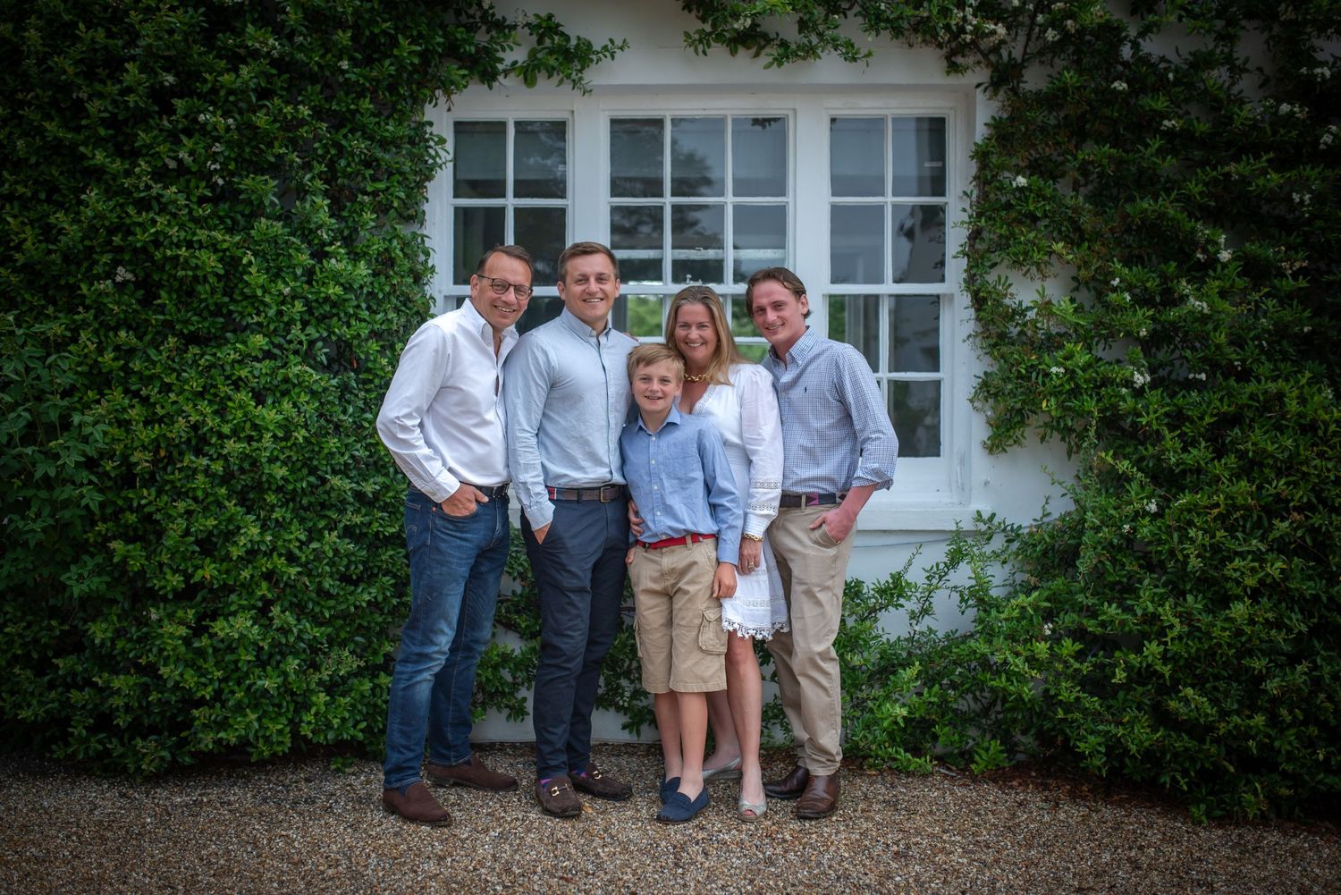 Family of five posing together outside a white cottage covered in green climbing plants family portrait