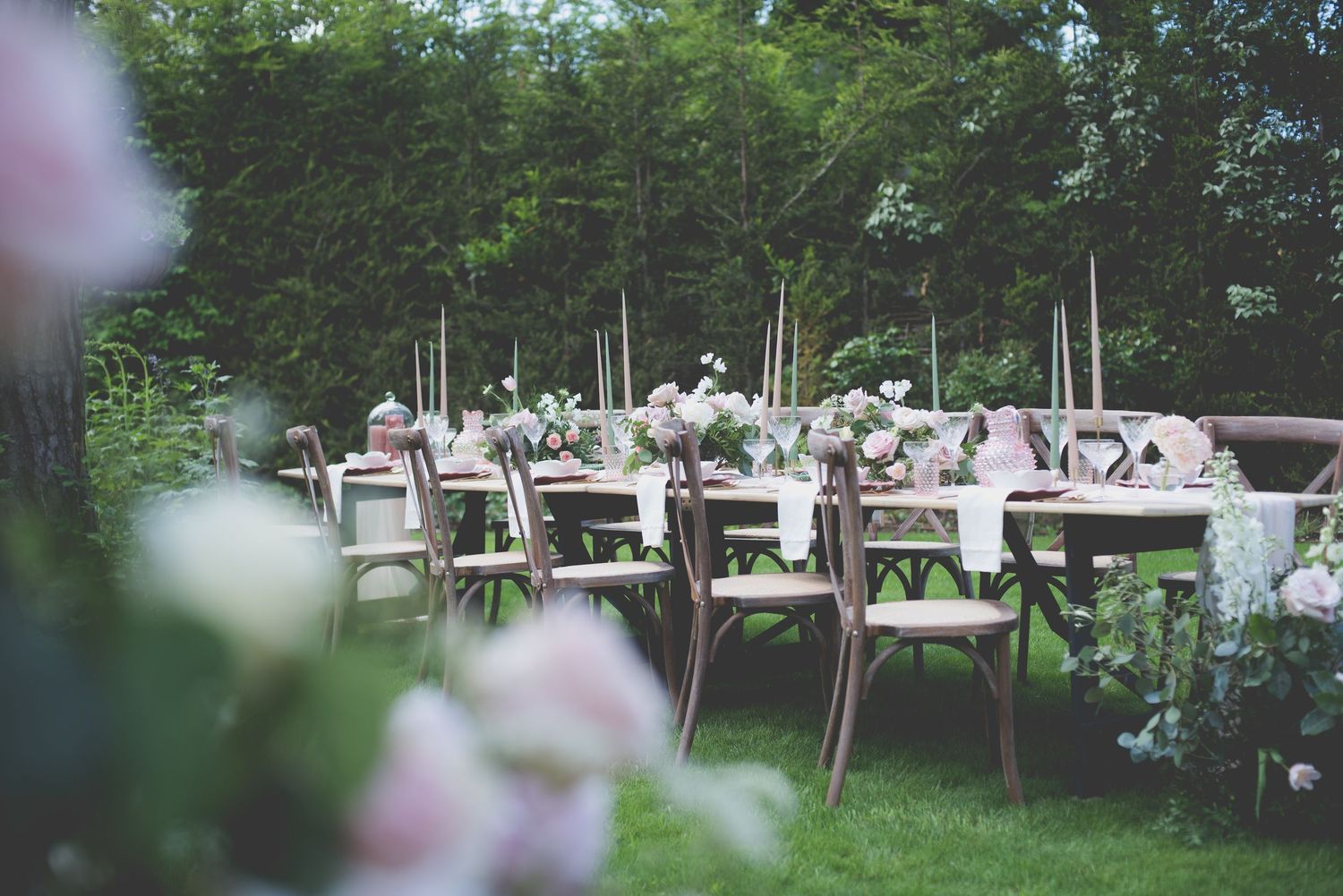 Romantic outdoor wedding reception tables with pink floral arrangements in a garden.