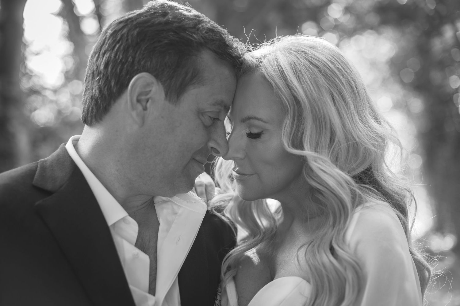 Intimate black and white portrait of couple touching foreheads in a romantic moment outdoors.