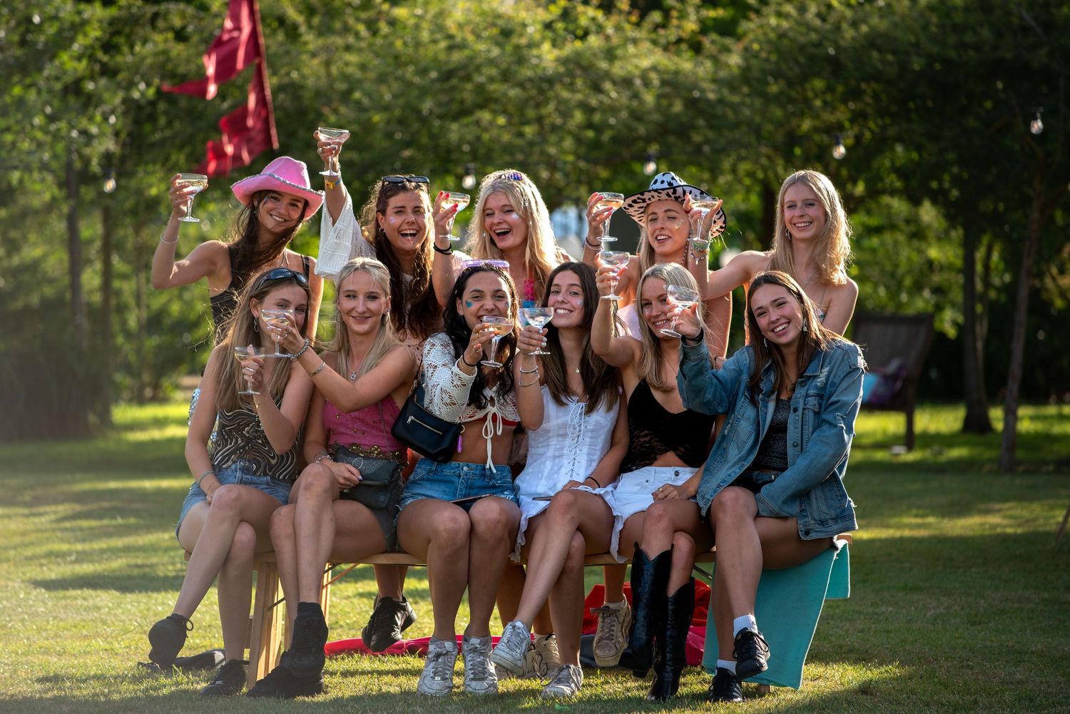 Group of young women celebrating outdoors raising glasses in a sunny garden party setting.