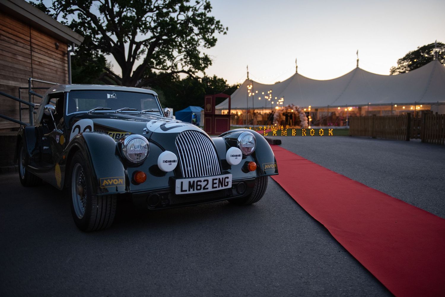 Classic Morgan sports car parked on red carpet at dusk outside Lambrook event marquee.