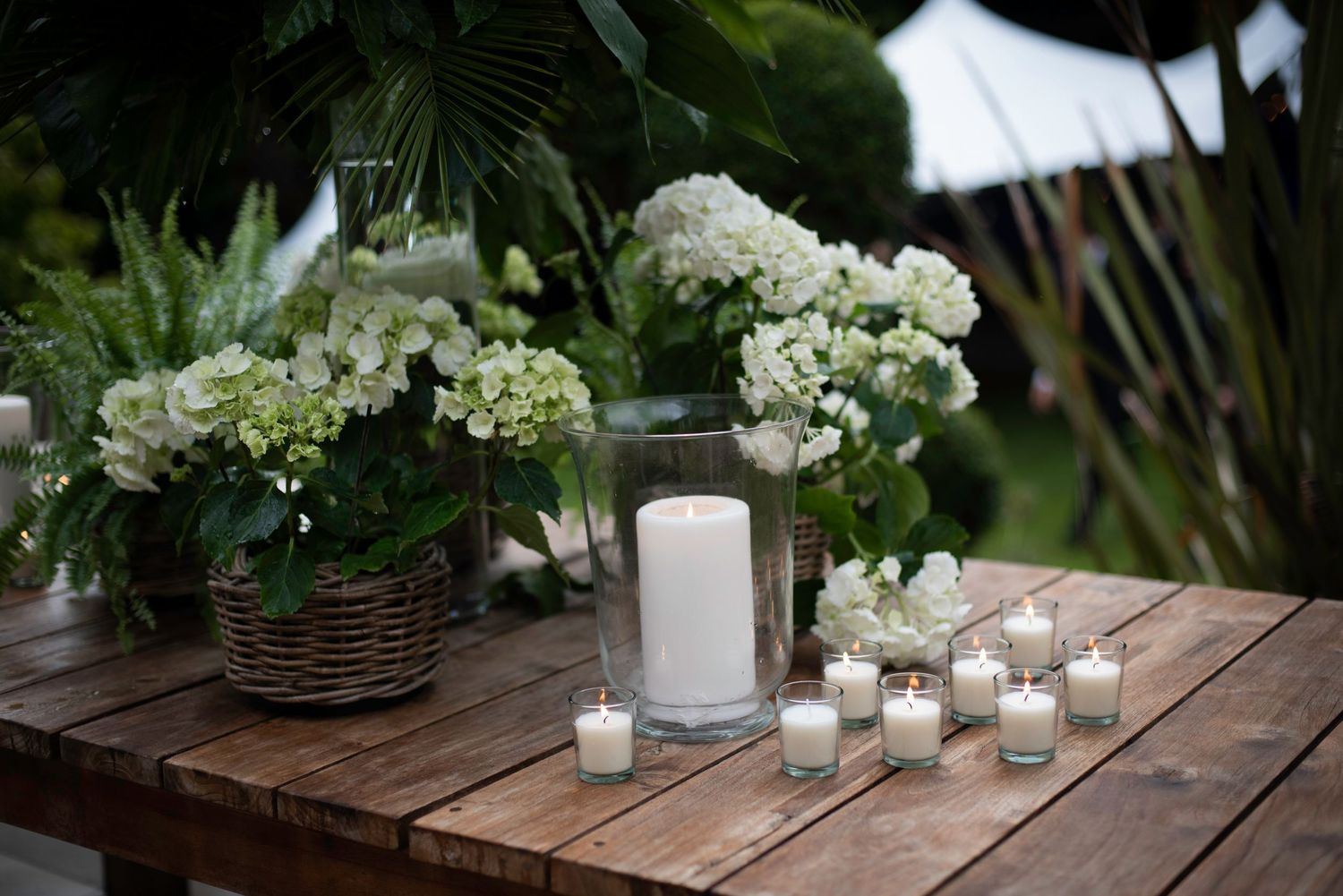 Rustic wooden table with white hydrangeas, pillar candle, and votive candles for wedding decor.