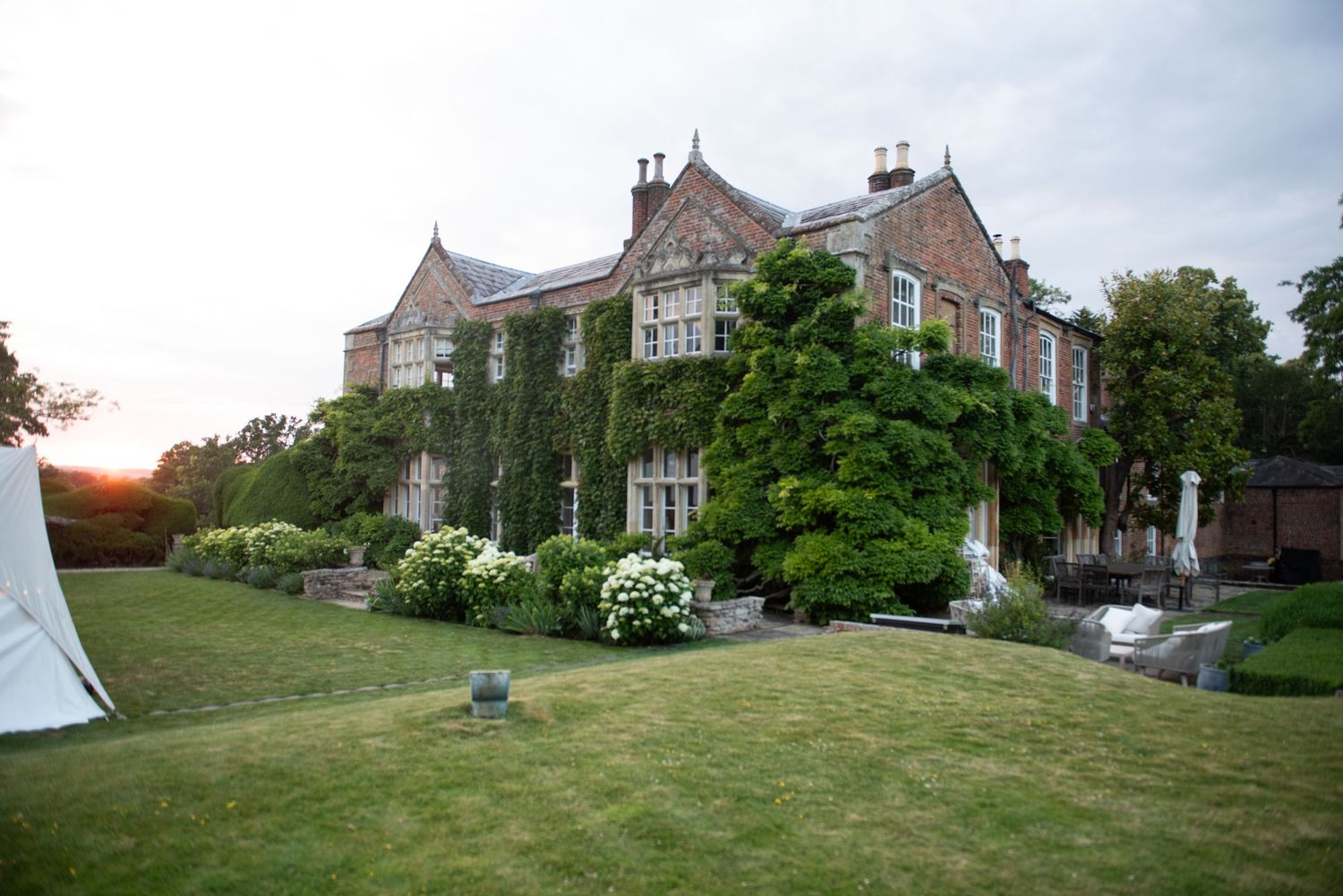 Grand ivy-covered Victorian manor house photographed at sunset during an outdoor wedding celebration.