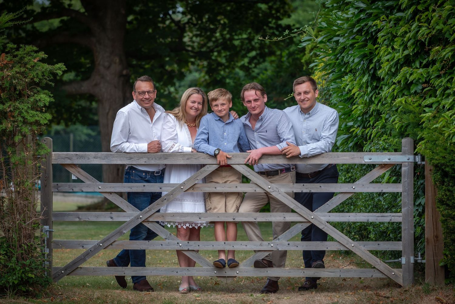Family of five posing together at wooden gate in countryside setting.