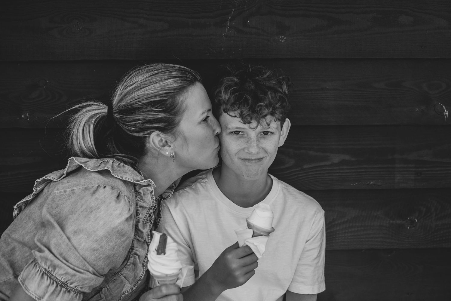 Black and white photo of mother kissing young boy on cheek while both hold ice cream cones.