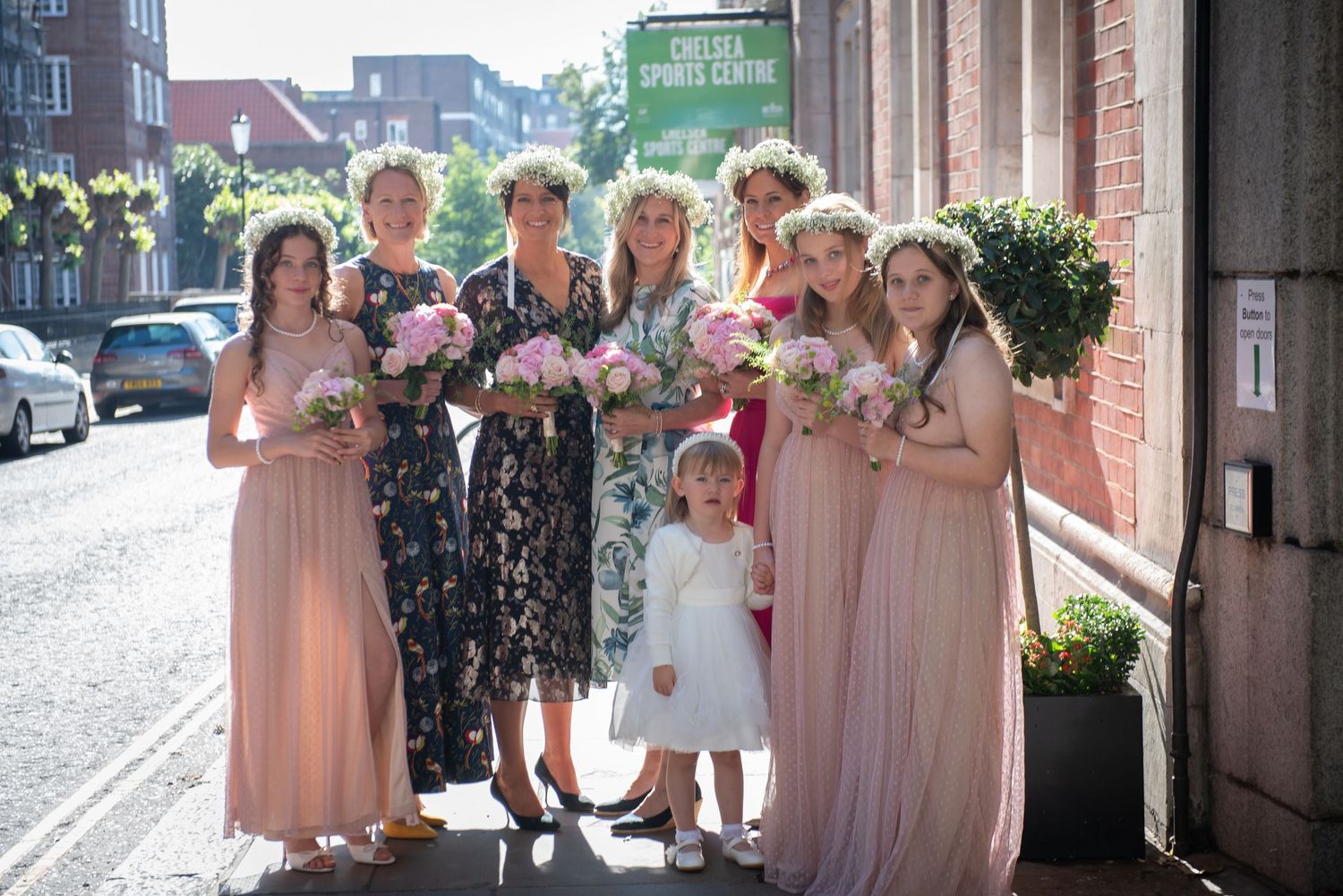 Group of bridesmaids in blush pink dresses with flower crowns holding bouquets outside Chelsea Town Hall Wedding.