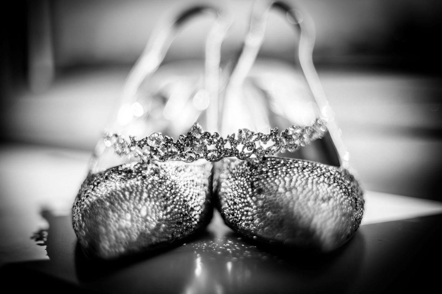 Close-up of sparkling crystal-encrusted bridal heels in black and white photography.