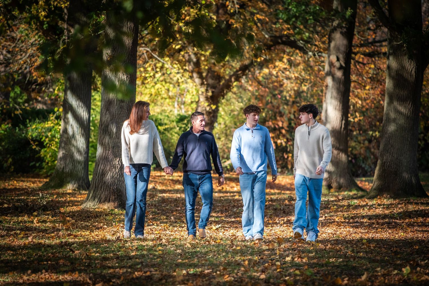 A family of four walks hand in hand through a beautiful autumn woodland park.