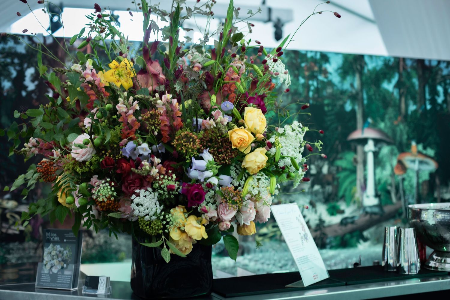 Lush colorful floral arrangement in black vase with roses and mixed blooms on display counter.