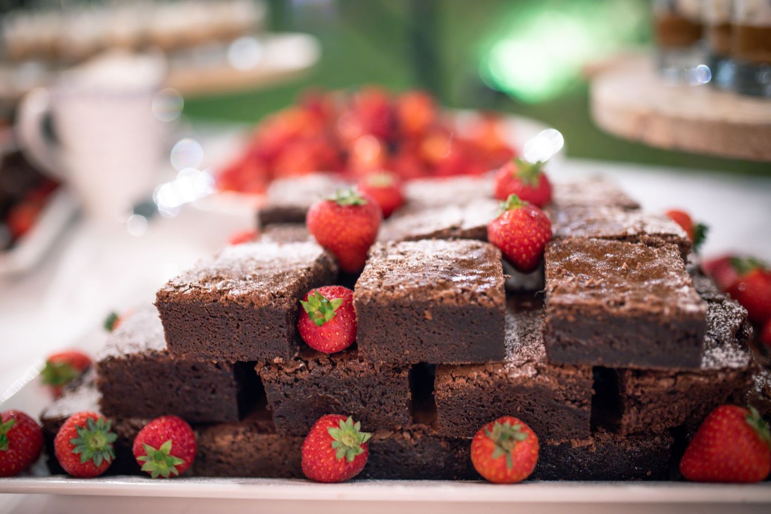 Stack of chocolate brownies garnished with fresh strawberries on white dessert table.
