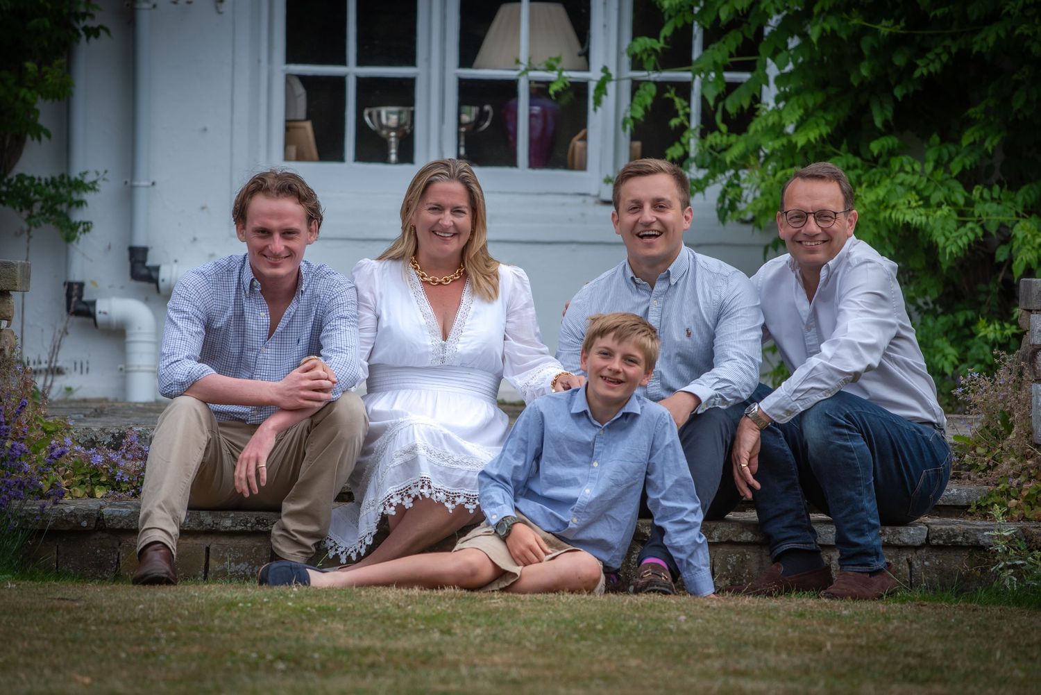 Family of five smiling together on garden steps outside a charming country house in summer.
