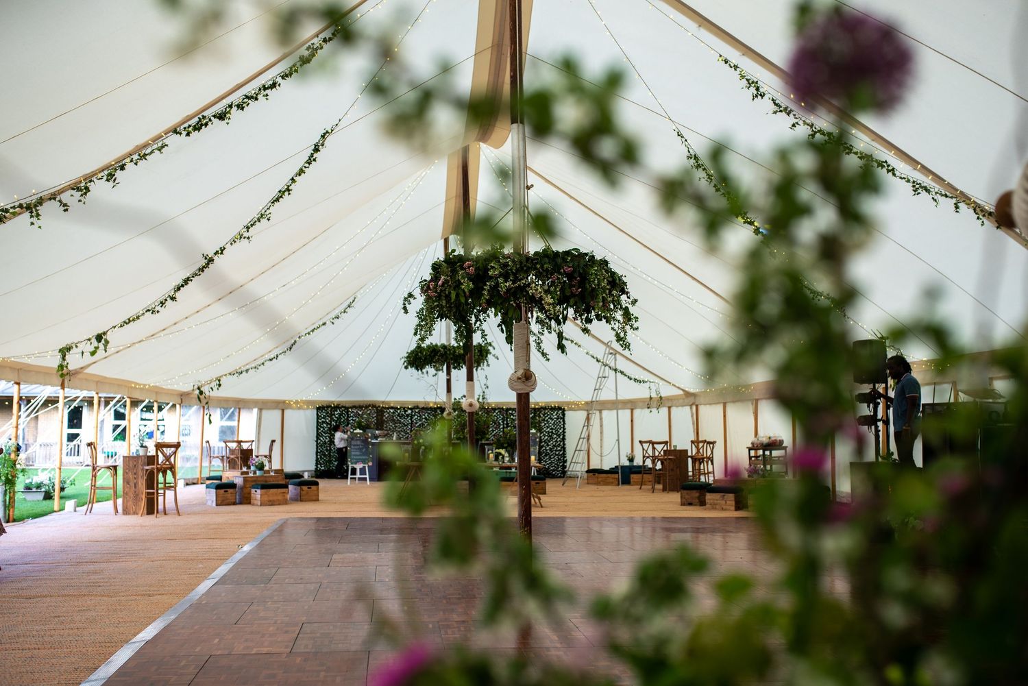Elegant marquee wedding reception interior with fairy lights, greenery decorations and wooden dance floor.