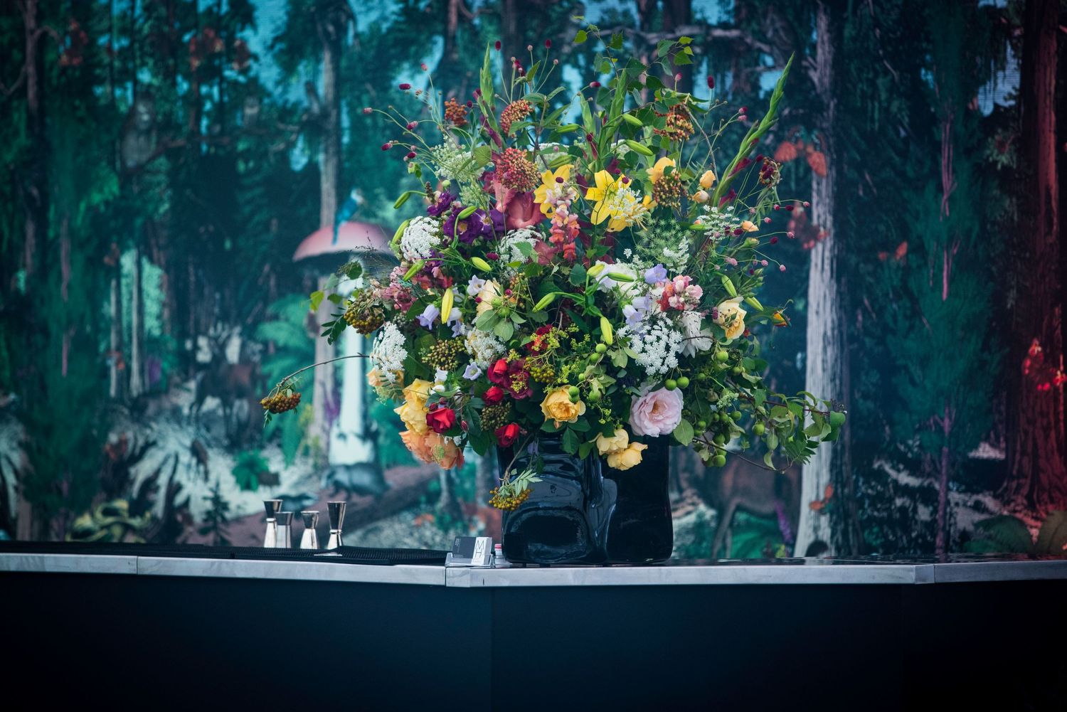 Vibrant floral arrangement with colorful blooms displayed against a painted forest backdrop.