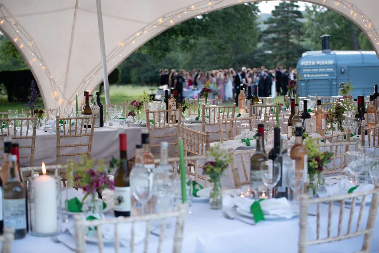 Elegant outdoor wedding reception under a marquee with fairy lights and floral centerpieces.