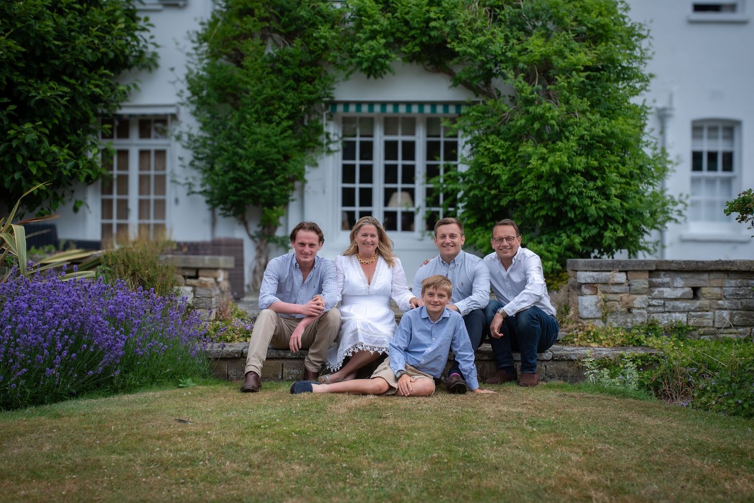 Family of five posing on a sunny lawn in front of a beautiful ivy-covered country home.