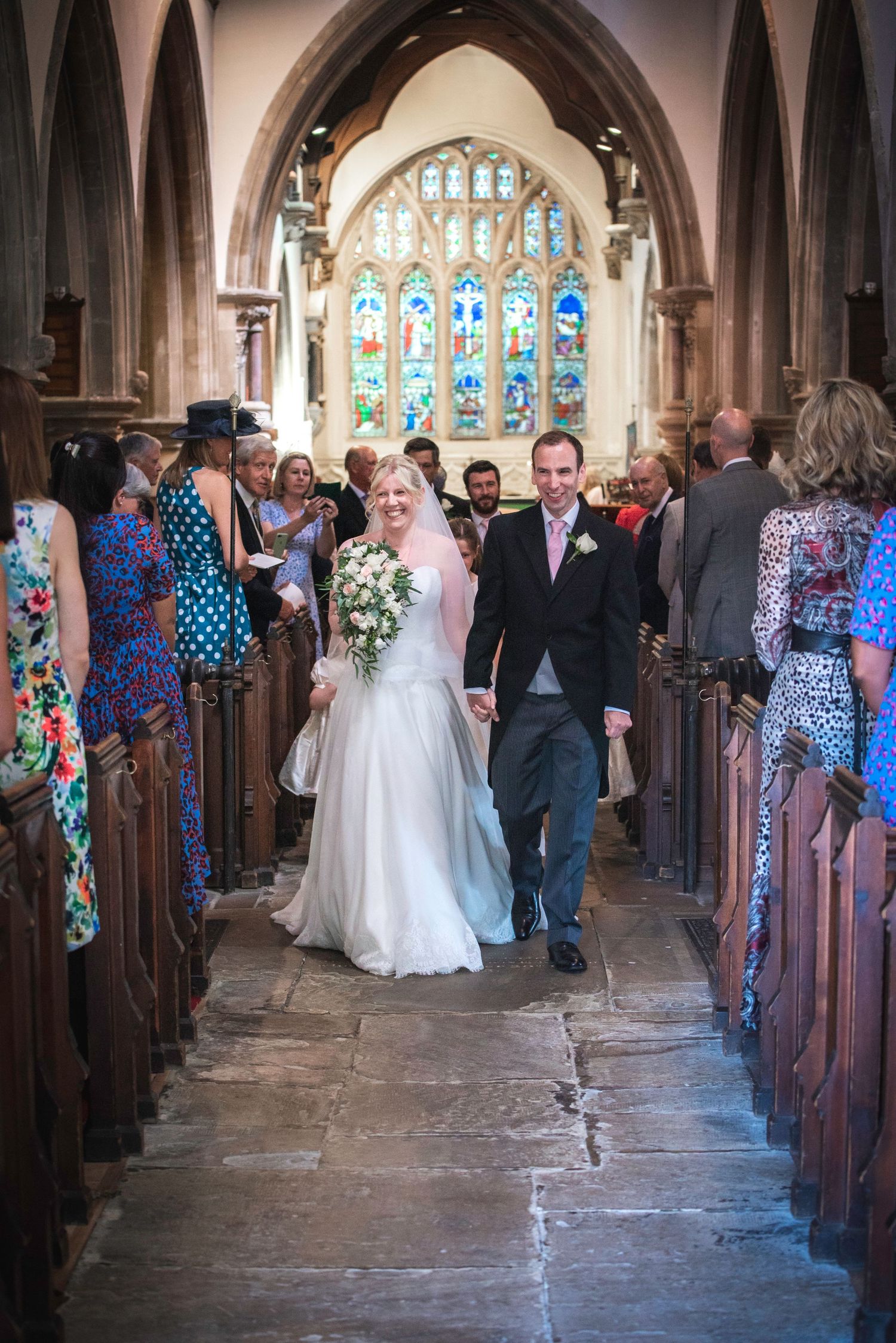 Newlywed couple walking back down church aisle smiling after wedding ceremony with guests watching. St Michaels Church Bray.