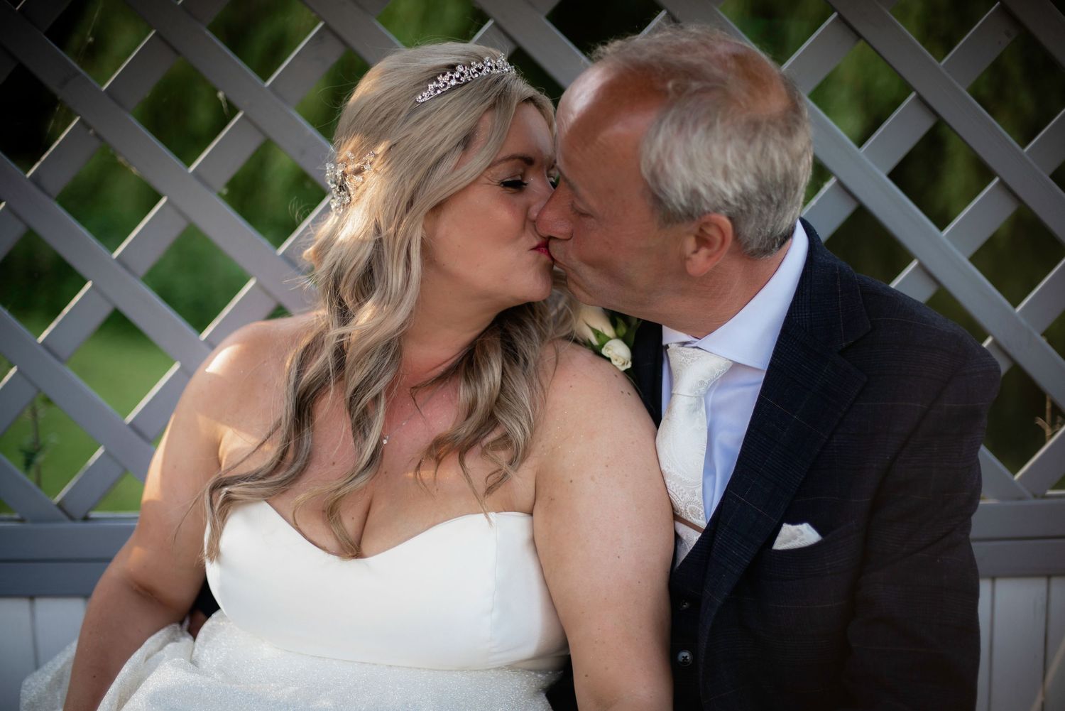 Bride and groom sharing a romantic kiss on their wedding day outdoors.