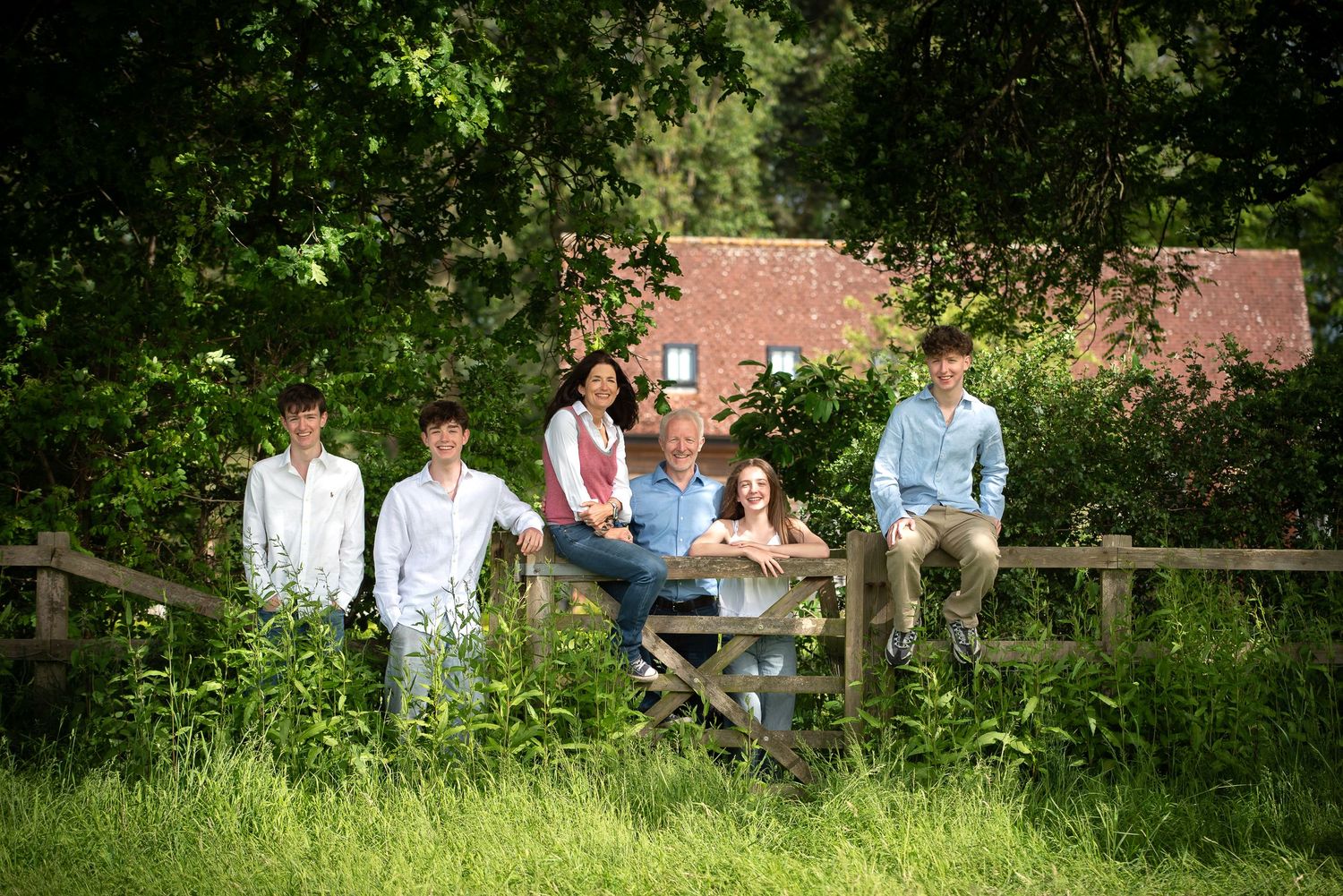 Family of six posing by a wooden fence surrounded by lush greenery. family portrait