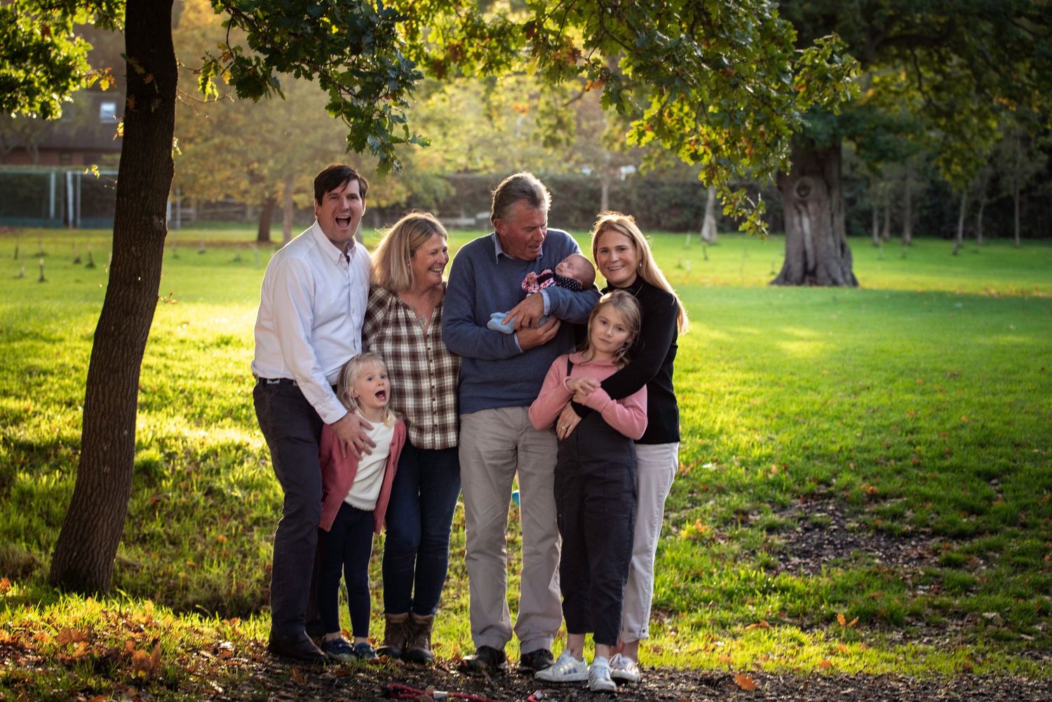 Happy multigenerational family gathering outdoors in autumn park with golden light.