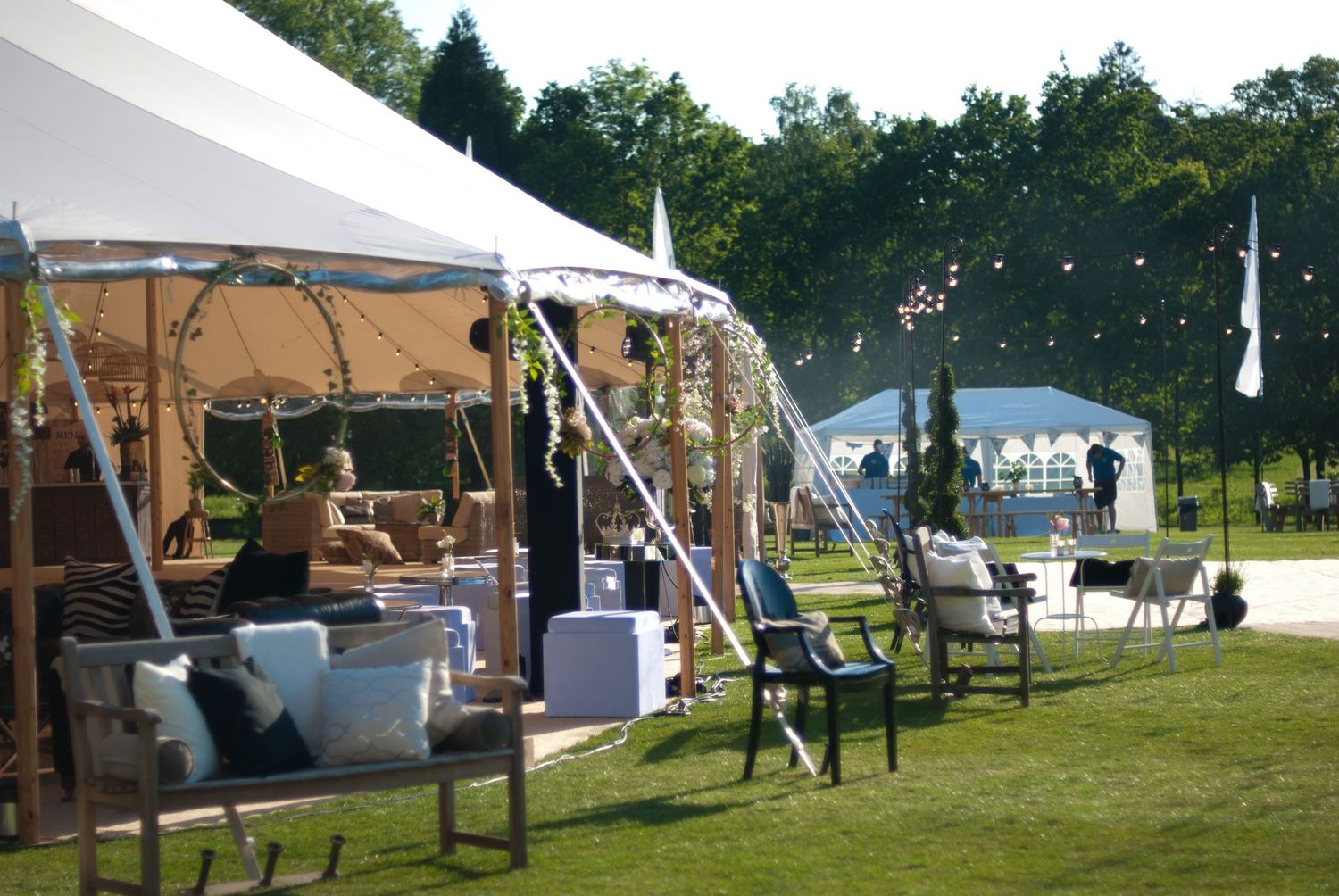 Outdoor wedding venue with white marquee tents, garden furniture, and decorative bunting on a sunny day.