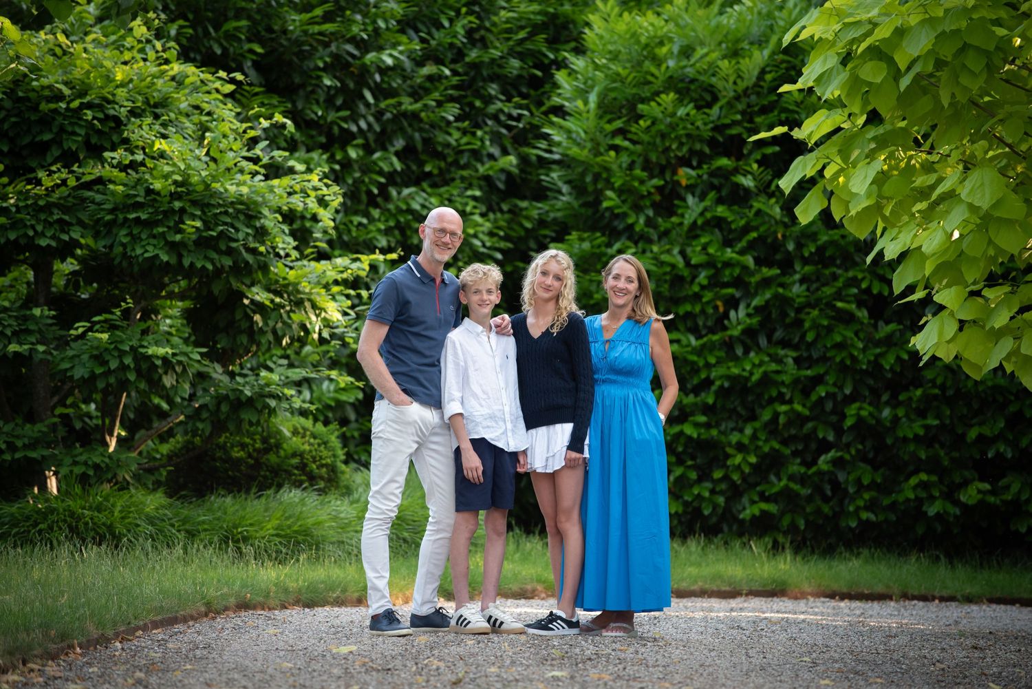 Family of four smiling together on a gravel path in a green garden. family portrait