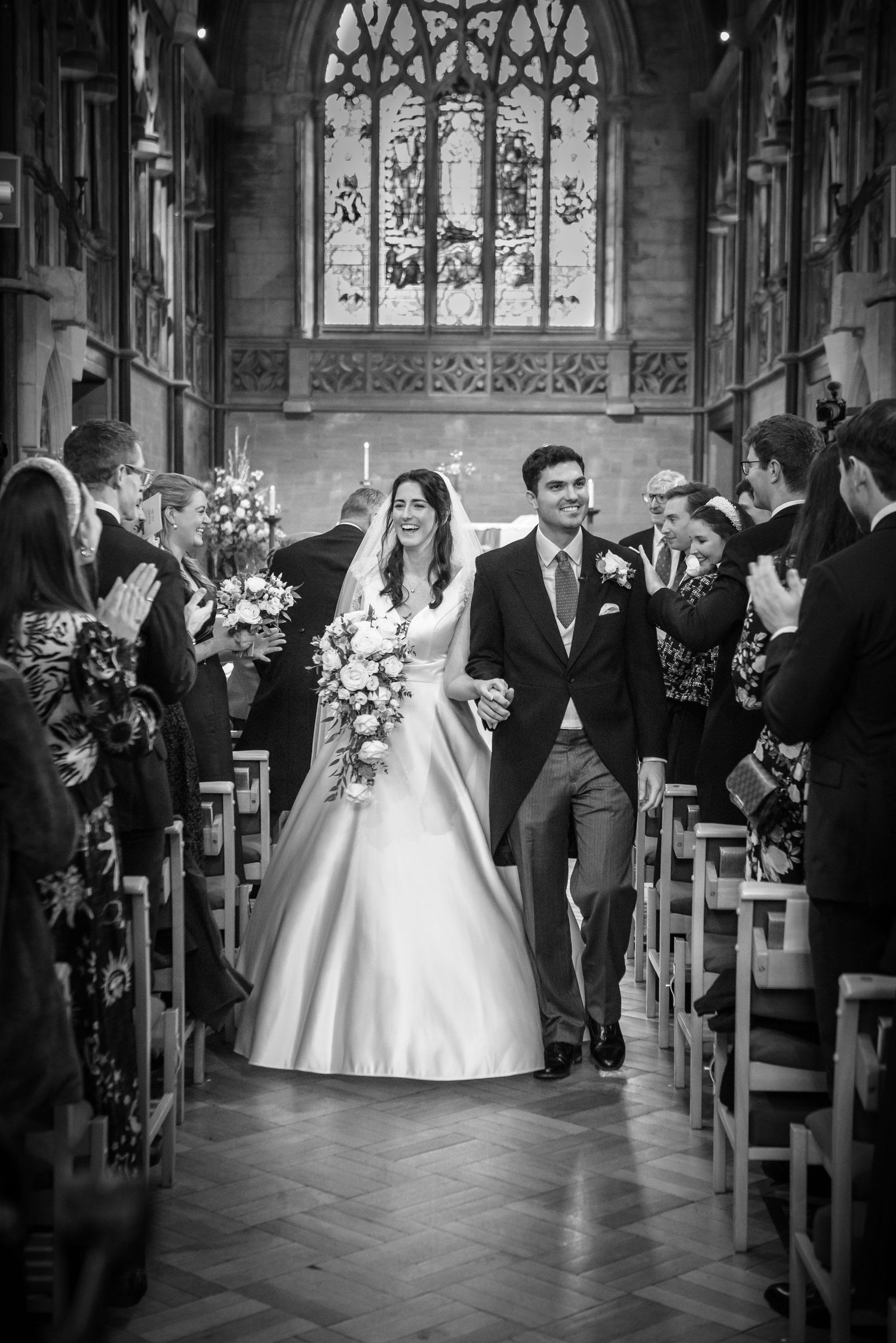 Black and white photo of a bride and groom walking down the aisle of a church after their wedding ceremony.