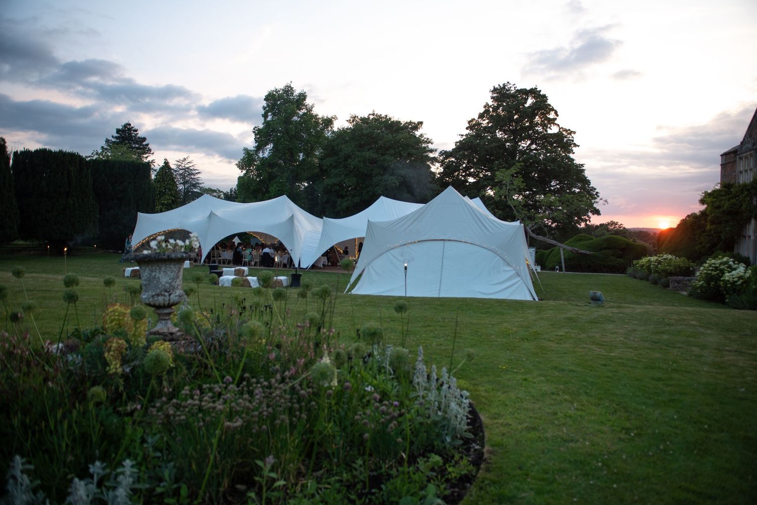 White stretch tent wedding marquee glowing at sunset in the gardens of a historic country estate.