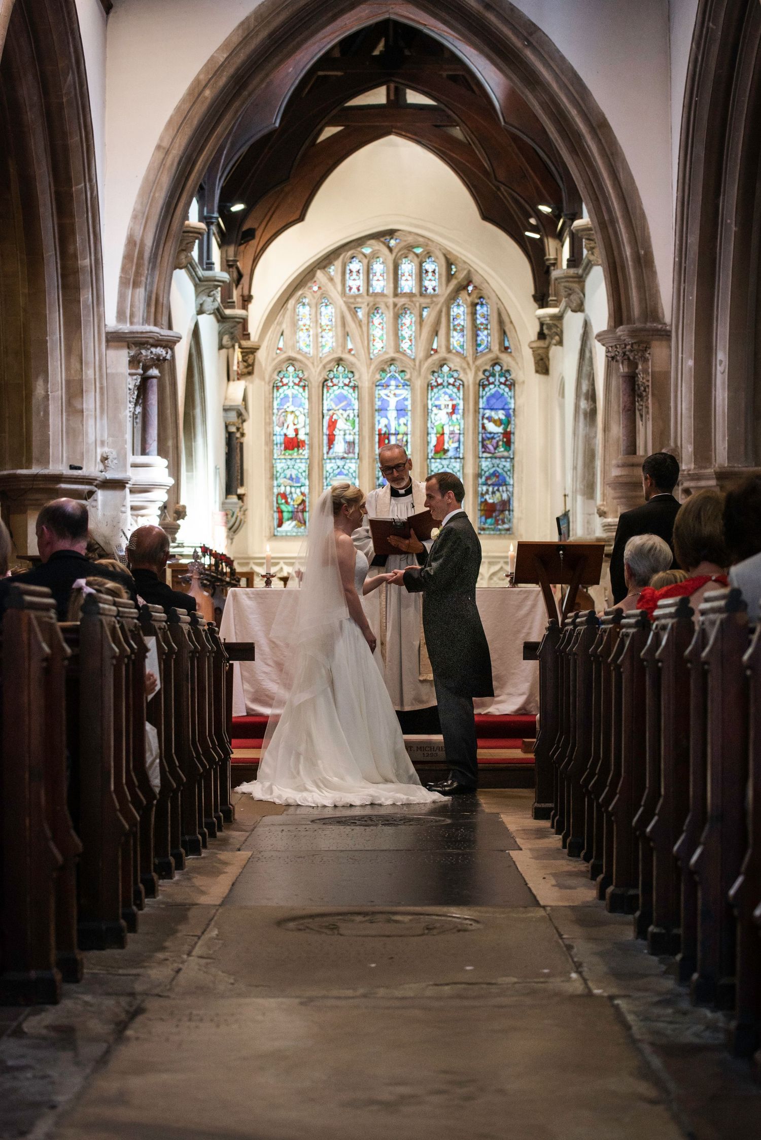 Bride and groom exchanging vows at church altar with stained glass windows and wooden pews. St Michaels Church, Bray