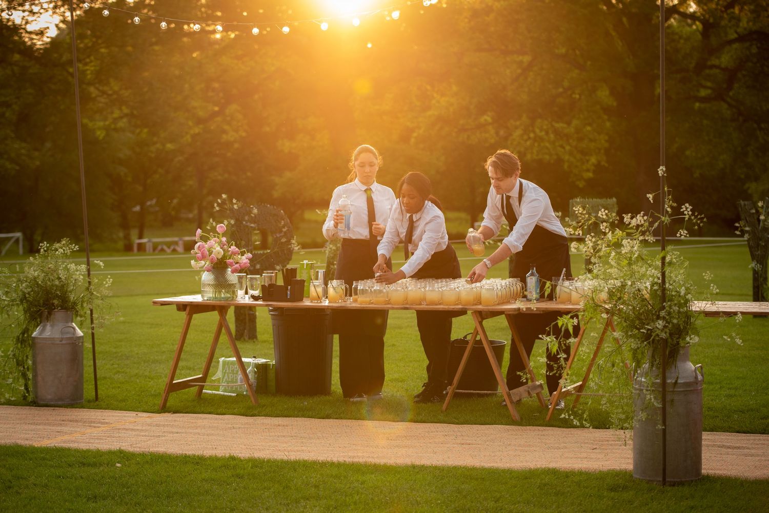Three servers preparing food at an outdoor banquet table bathed in golden sunset light.
Event and catering set up.