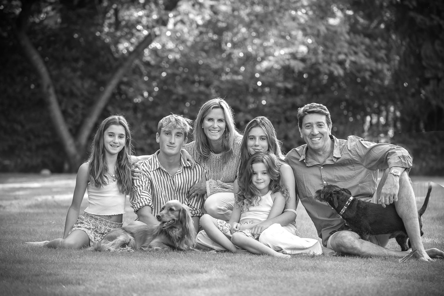Happy family of six relaxing on grass with dog in black and white outdoor garden portrait. Family portrait