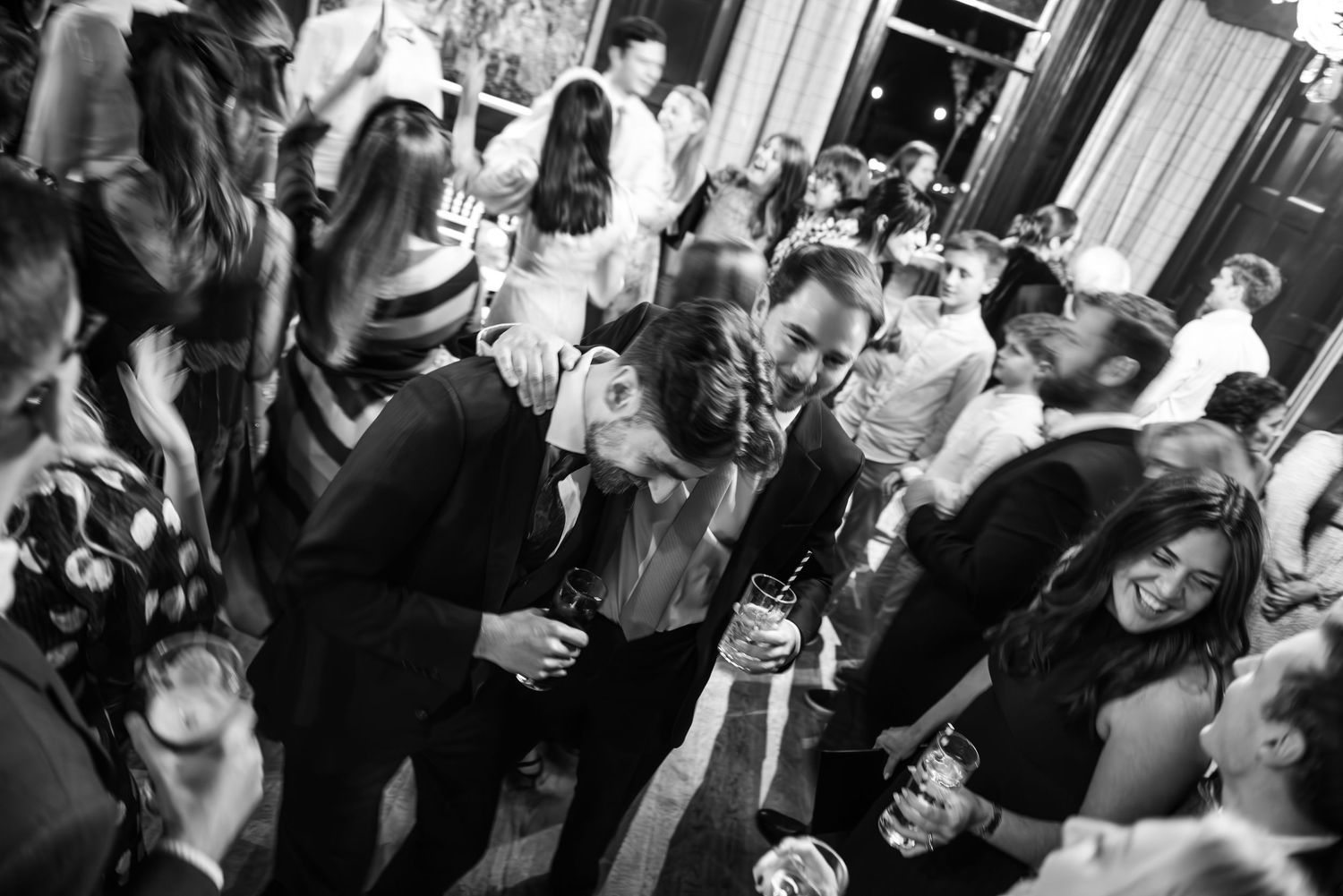 Black and white photo of wedding guests dancing and socializing at a lively wedding reception party.