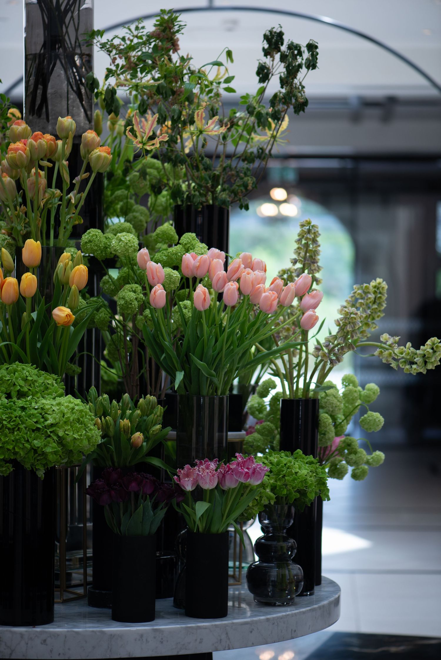 Stunning indoor floral arrangement with pink tulips, green viburnum, and mixed blooms in sleek black vases.  Fairmont Hotel, Windsor